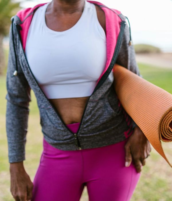 Woman in activewear smiling and stretching outdoors at sunrise.